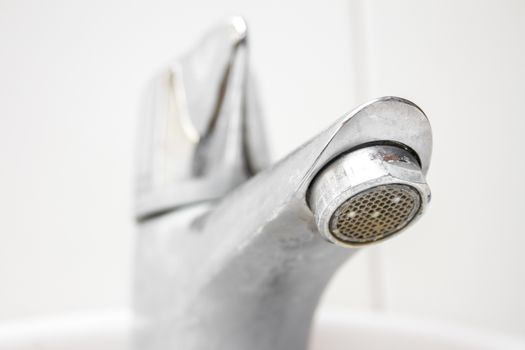 Modern style dirty faucet closeup view on white tiles background, small depth of field