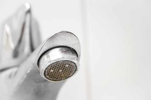 Modern style dirty faucet closeup view on white tiles background, small depth of field