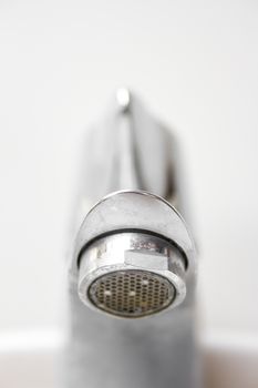 Front view of modern style dirty faucet closeup view on white tiles background with small depth of field