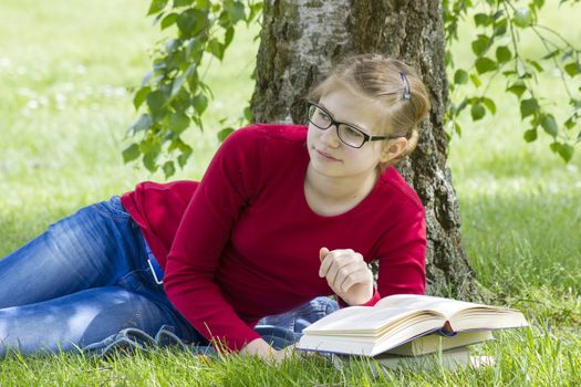 Young girl reading book in park in spring day