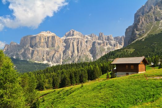 summer landscape in Fassa Valley with a small chalet beneath Dolomites mountains, Trentino, Italy