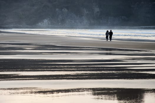 Romantic couple walking on the beach. Sunset in backlight.