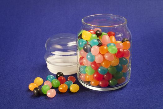 Open jar of multi colored Jelly Beans. Blue background.