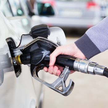 Petrol or gasoline being pumped into a motor vehicle car. Closeup of man pumping gasoline fuel in car at gas station.