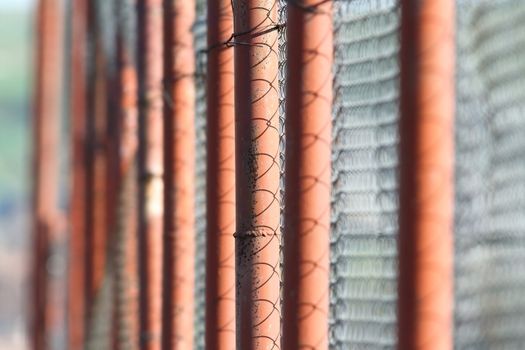 perspective view of rusty metal fence made with pillars painted brown and wire