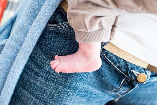 mother carrying her little baby - naked foot of newborn against bluejeans with golden button for size comparison