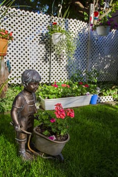 Bronze statue of a boy pushing a trolley of flower in a garden