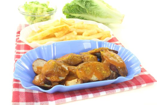Currywurst with french fries on a napkin before light background