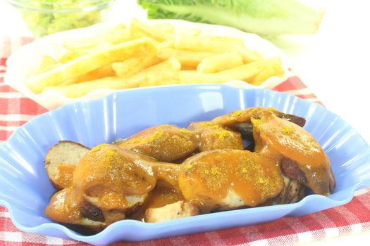 Currywurst with french fries on a checkered napkin before light background