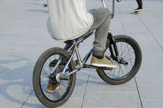 fragment of guy with sports clothing sit on sports BMX bicycle on grey urban concrete background