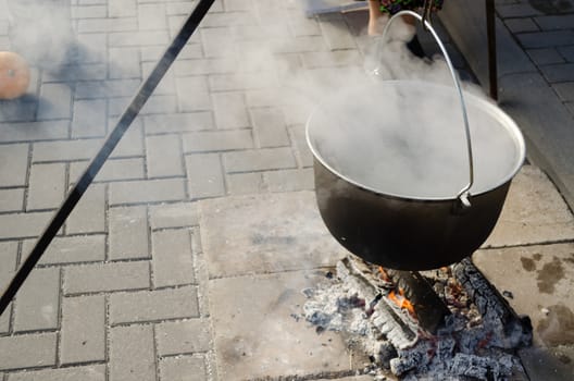 large antique old pot on metal rods strongly vaporize on fire outdoors