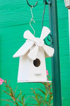 A cute white bird house hanging on the pole.