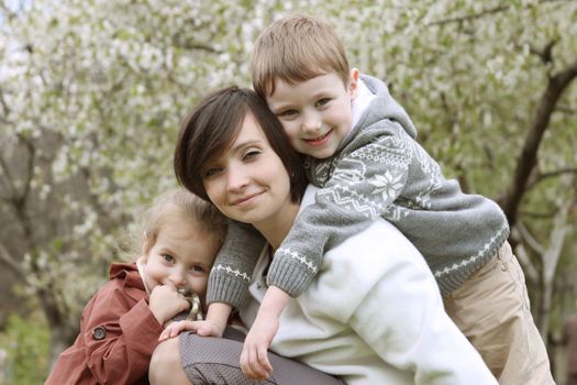 Happy mother and two children hugging among blooming garden