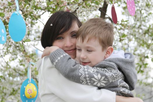 Happy mother and son in blooming garden decorating for Easter