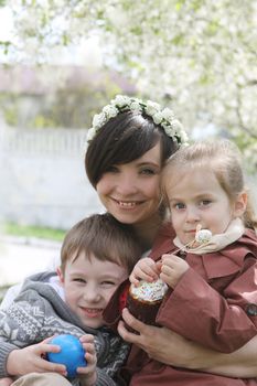 Happy mother and two children with Easter cake hugging among blooming garden