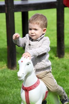 2 years old Baby boy playing with horse on playground 