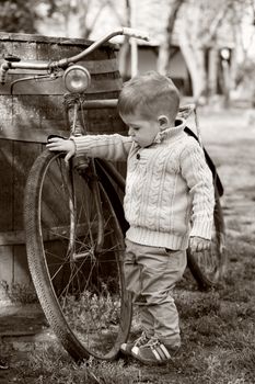 2 years old curious Baby boy walking around the old bike on sepia brown color