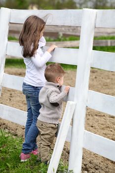 Pre-teen girl and Baby boy on the a white picket fence beside the horse