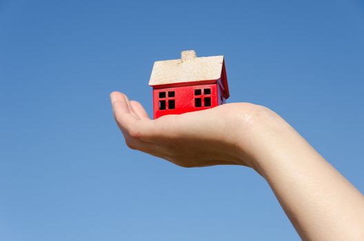 red small iron house toy miniature in female palm on blue sky background