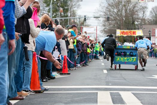 Lawrenceville, GA, USA - March 29, 2014:  Spectators cheer on a team pushing a bed toward the finish line of the annual Lawrenceville Bed Race, to benefit a local Gwinnett County homeless shelter.
