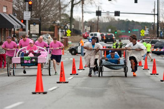 Lawrenceville, GA, USA - March 29, 2014:  Two teams push silly looking beds through downtown streets in the annual Lawrenceville Bed Race, to benefit a local Gwinnett County homeless shelter.