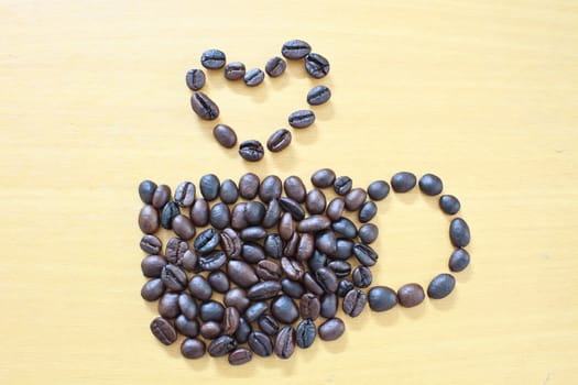 Coffee cup with heart image made up of coffee beans on wood background
