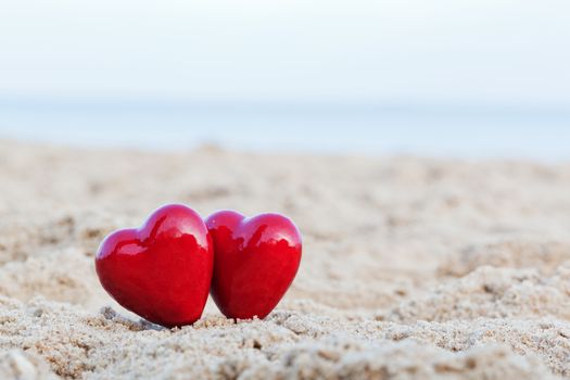 Two red hearts on the beach symbolizing love, Valentine's Day, romantic couple. Calm ocean in the background