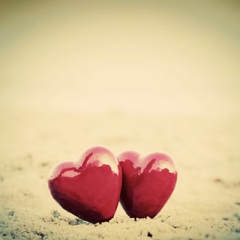 Two red hearts on the beach symbolizing love, Valentine's Day, romantic couple. Calm ocean in the background. Vintage, retro style