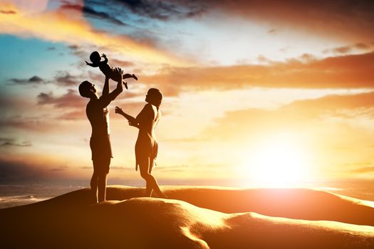 Happy family together, parents celebrating their little child by the seaside at sunset, summer time. Birth, mother, father concepts 