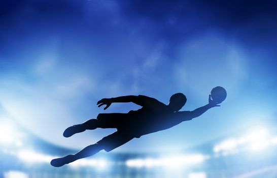 Football, soccer match. A goalkeeper jumping to defend, save the ball from goal. Lights on the stadium at night.