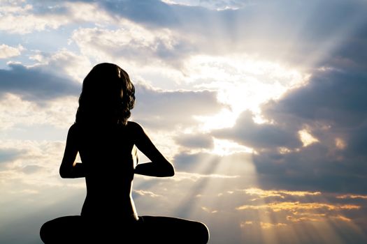 A silhouette of a woman sitting in yoga position, meditating against sunset sky. Zen, meditation