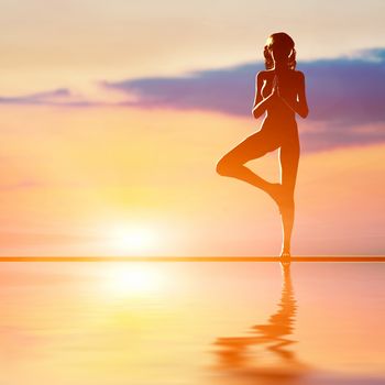 A silhouette of a woman standing in tree yoga position, meditating against sunset sky. Zen, meditation