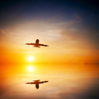 Airplane taking off at sunset. Silhouette of a big passenger or cargo aircraft, airline flying. Abstract water reflection. Transportation