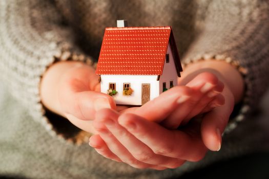 Woman holding a small new house in her hands. Real estate, mortgage, housing concepts etc.