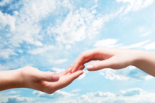 Man and woman hands touch in gentle, soft way on blue sunny sky. Concepts of connection, hope, faith, help, love.