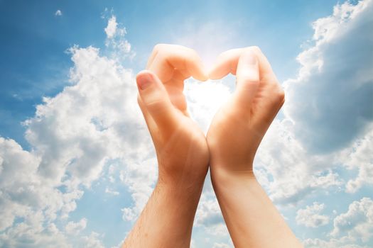 Man and woman hands make a heart shape on blue sunny sky. Love, emotions, happiness.