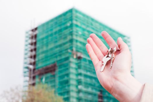 A real estate agent holding keys to a new apartment in her hands. Building under construction Real estate industry