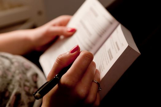 Close-up of a woman hands taking notes in a book while studying at home lying on bed