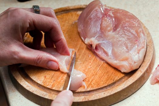 Cutting meet in slices on a wooden board. Woman hands close up.