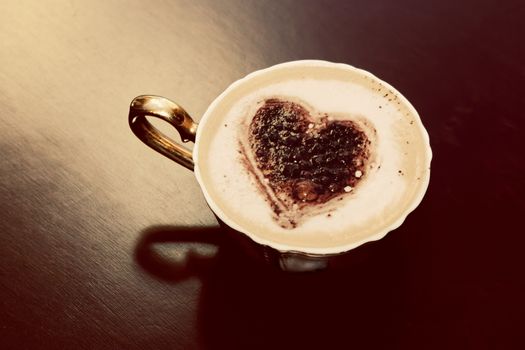 Cup of coffee with chocolate heart shape on milk foam. Romantic morning light. Vintage