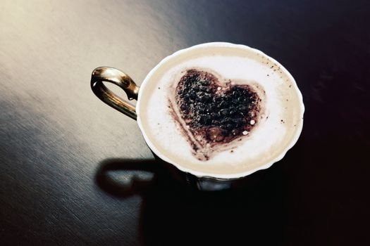 Cup of coffee with chocolate heart shape on milk foam. Romantic morning light.