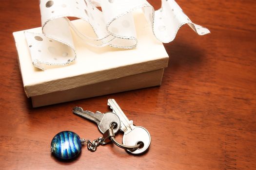 Two keys lying next to a cream colored gift box