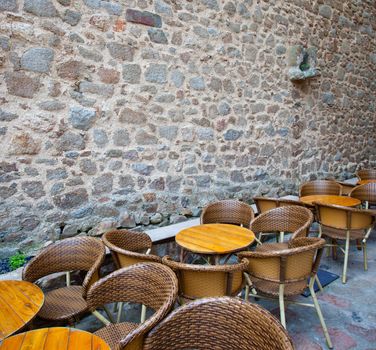 tables and wicker chairs in summer cafe near the ancient stone wall