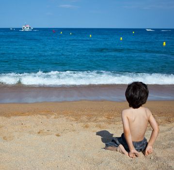 boy sitting on the shore looking at the blue sea