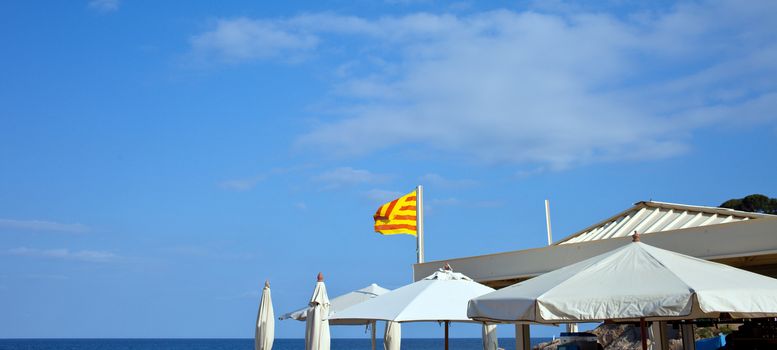 White umbrellas and the flag of Catalunya under a blue sky on the beach