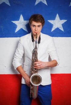 Studio portrait of young cool man with saxophone on American flag background.