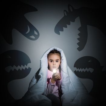 image of a girl under the covers with a flashlight the night afraid of ghosts