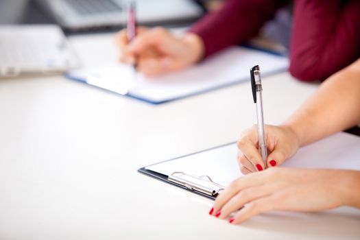 Woman at class desk holding a written examination with shallow focus on pen