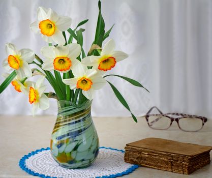 Beautiful large flowers of narcissuses in a vase on a table near the ancient book.