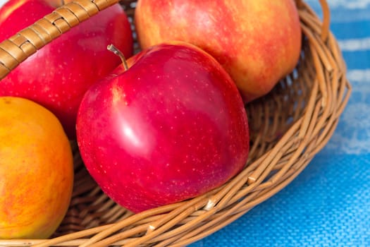 Large ripe apples are in a wattled basket on a table.